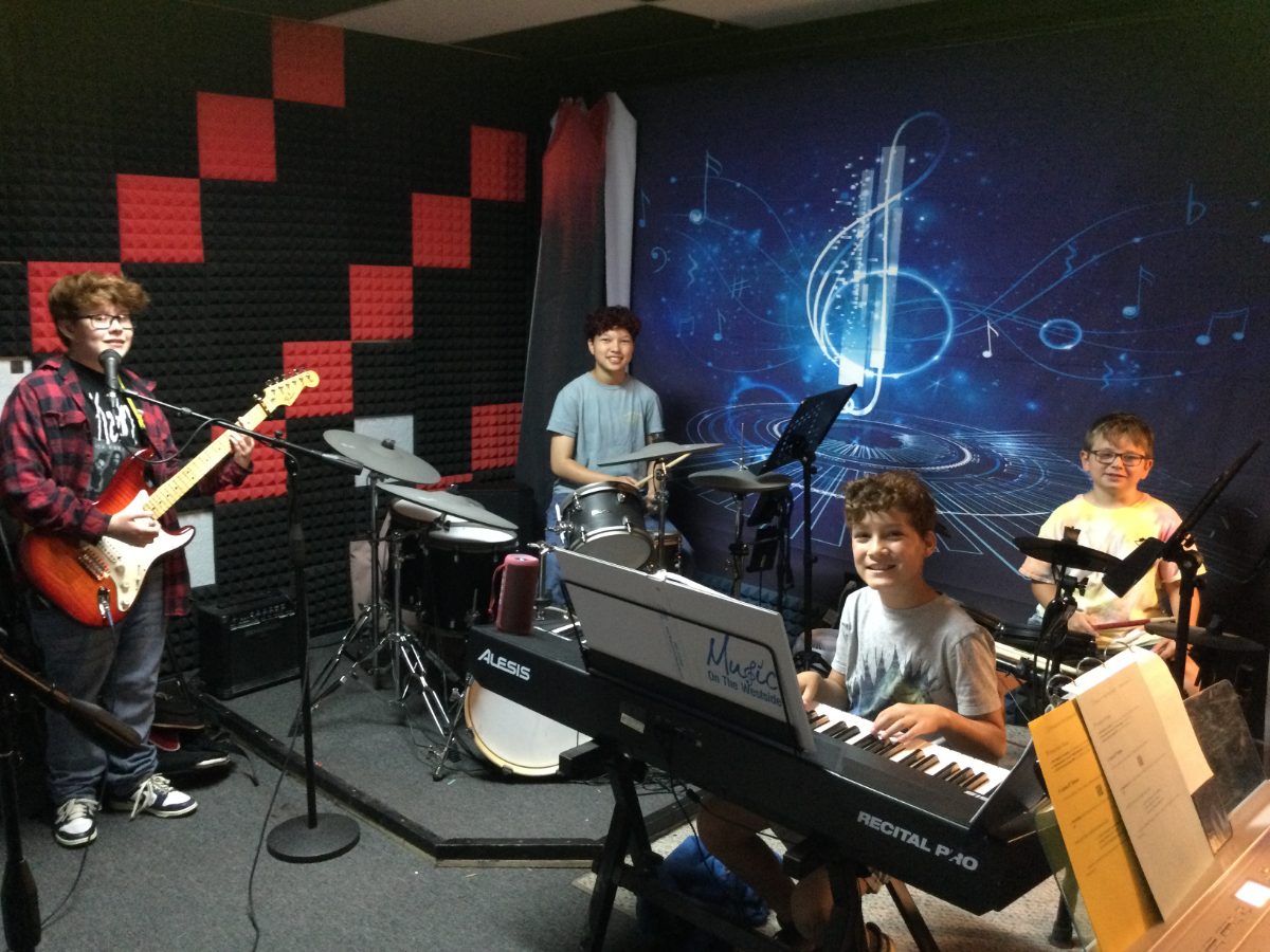 Student band playing guitar, drums and keyboard in the Music on the Westside practice room